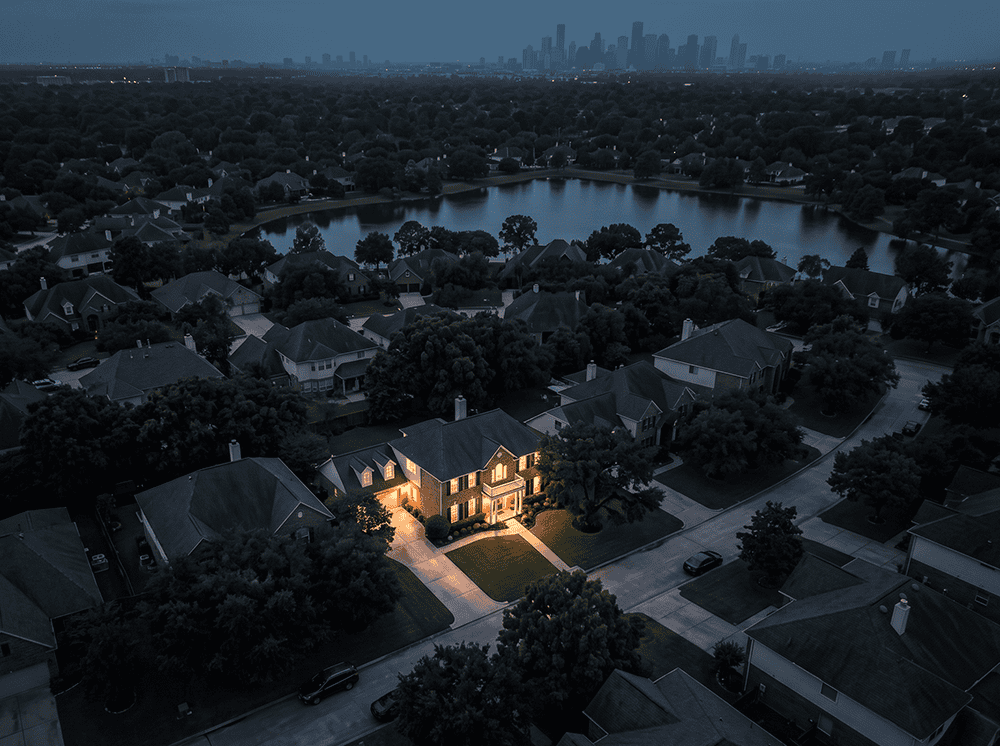 Aerial view of a dark neighborhood at dusk with one home fully lit