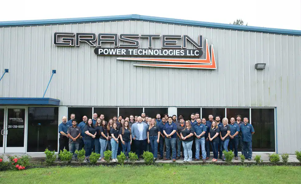 The Grasten team standing outside the Grasten Power Technologies building, under the company sign